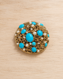 Blue cabochon pearl and rhinestone brooch on wood table