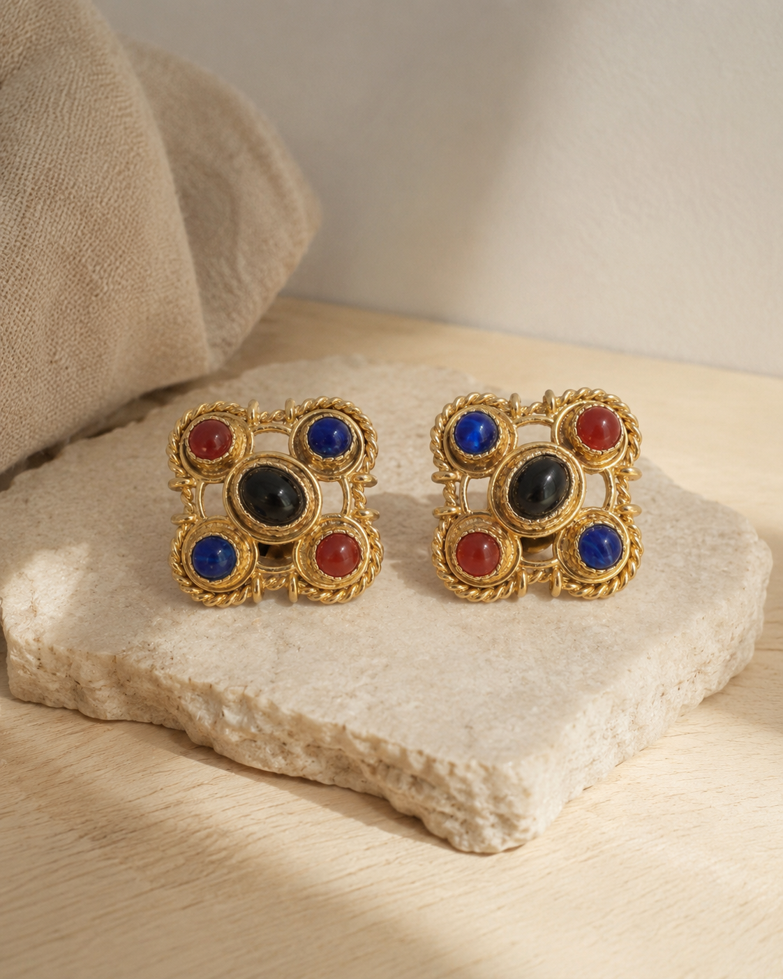 Pair of gem-tone clip earrings on a pale stone surface