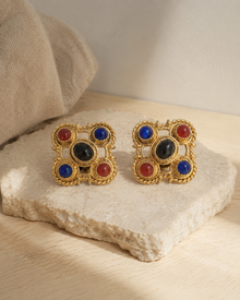 Pair of gem-tone clip earrings on a pale stone surface
