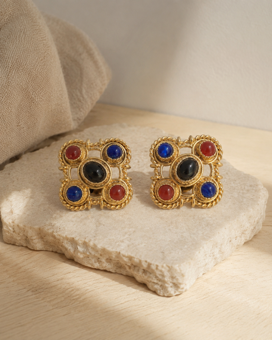 Pair of gem-tone clip earrings on a pale stone surface