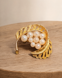 Gold-tone leaf faux pearl brooch on wood table