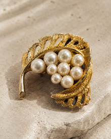 Close detail of gold-tone leaf faux pearl brooch on stone