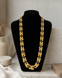 Gold-tone leaf and pearl necklace displayed on a black bust