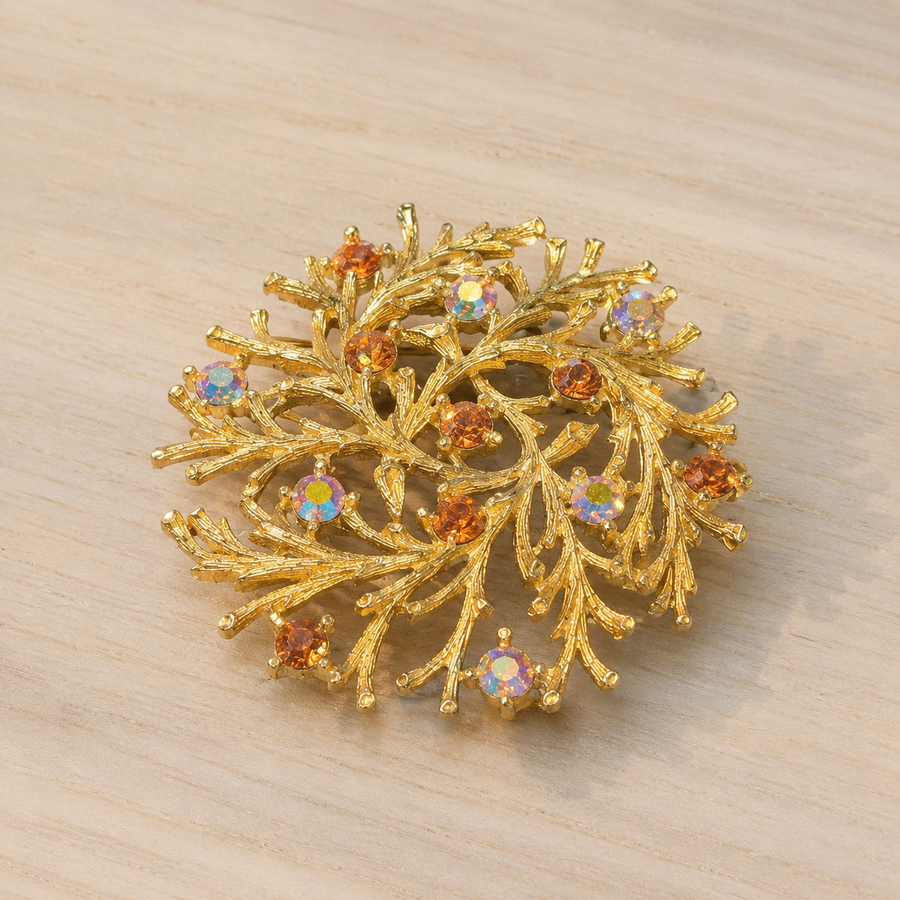 Gold-tone branch rhinestone brooch on wood table