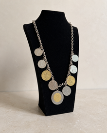 Angled view of Italian lire-style coin charm necklace on display stand