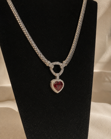Silver-tone necklace with red heart pendant on black display bust