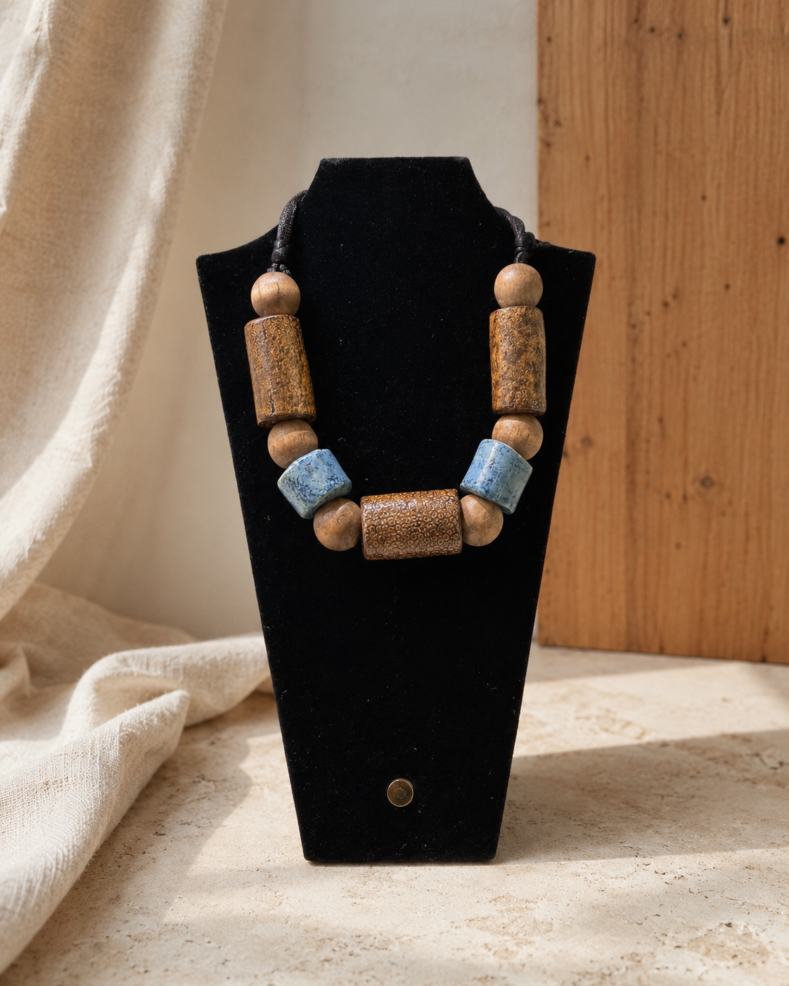 Wood and blue ceramic bead necklace displayed on a black bust